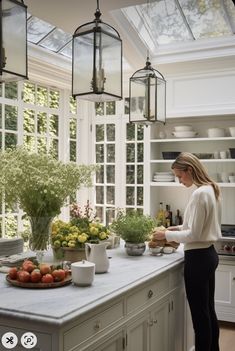 a woman standing in a kitchen preparing food on top of a white counter next to a potted plant