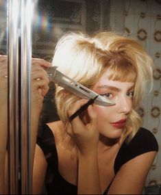 a woman holding a pair of scissors up to her face in front of a mirror