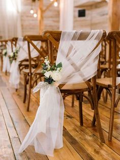 a row of wooden chairs with white sashes and flowers tied to the back of them