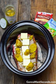 a crock pot filled with food sitting on top of a wooden table next to some butter