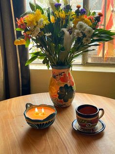 a vase filled with flowers sitting on top of a table next to a cup and saucer