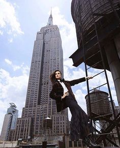 a woman standing in front of a tall building with her arms outstretched and legs spread out