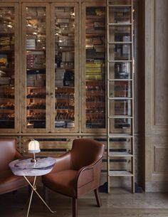 two brown chairs sitting next to each other in front of a book case filled with books