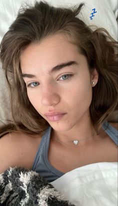 a young woman laying in bed with her nose open and looking at the camera while holding a teddy bear