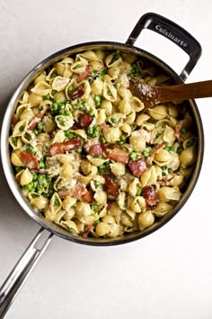 a pan filled with pasta and peas on top of a white counter next to a wooden spoon