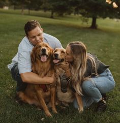 a man and woman sitting in the grass with two dogs, one brown and one tan