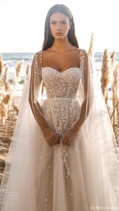 a woman in a wedding dress standing on the beach with her arms behind her back