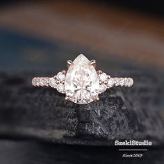 an engagement ring with a pear shaped diamond in the center on top of a rock