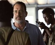 a man with glasses talking to another man in front of him on the set of captain phillips