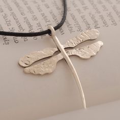 a silver dragonfly pendant sitting on top of an open book