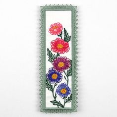 an embroidered bookmark with flowers and leaves on it's edge, hanging from a wall