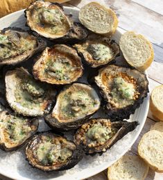 a white plate topped with lots of oysters next to slices of baguette bread