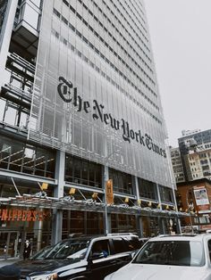 the new york times building is surrounded by parked cars and tall buildings in the background