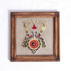 an embroidered piece in a wooden frame with beads and tassels hanging from it