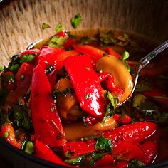 a bowl filled with red peppers and other vegetables next to a wooden spoon on top of a table