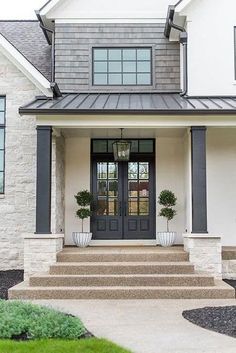 the front door of a house with two potted plants on each side and steps leading up to it