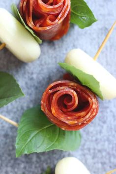 several pieces of food on sticks with leaves and sauces in them sitting on a gray surface