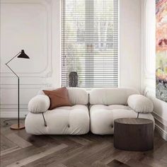 a white couch sitting in front of a window next to a wooden table and lamp