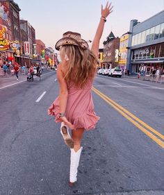 a woman is walking down the street with her arms in the air while wearing a hat