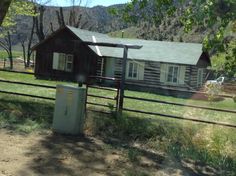 a log cabin sits in the middle of a field near a fence and a house