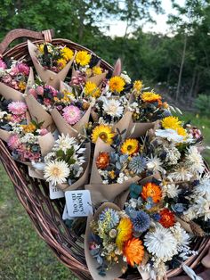 a basket filled with lots of different flowers on top of a grass covered field next to trees