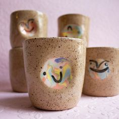 three cups with faces painted on them sitting next to each other in front of a pink wall