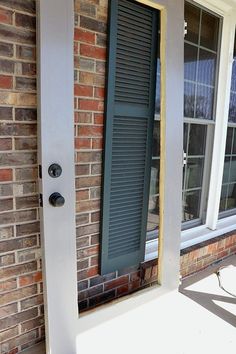 an open window on the side of a brick building with green shutters and white trim