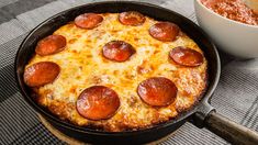 a pepperoni pizza in a skillet next to a bowl of chili and bread