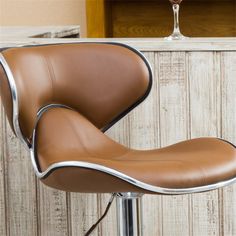 a brown and silver bar stool with a wine glass on the backrest in front of a wooden paneled wall