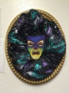 a purple mask with green and yellow paint on it's face in a circular gold frame