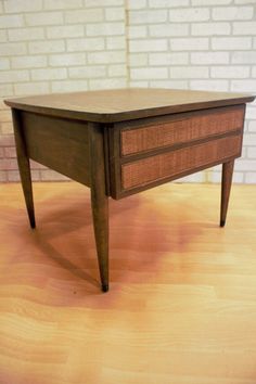 a small wooden table with drawers on it's sides, against a white brick wall