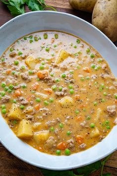 a white bowl filled with soup and potatoes on top of a wooden table next to some parsley