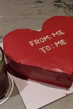 a red heart shaped cake with writing on it next to a cup of coffee and a candle