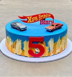 a blue birthday cake with cars on it and the number five in front of it