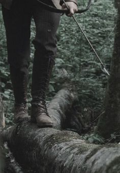 black and white photograph of a man with an arrow on a fallen tree in the woods