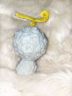 a white stuffed animal with a yellow cord on it's neck sitting in a pile of fur