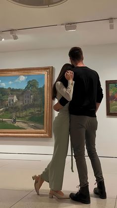 a man and woman standing next to each other in an art gallery looking at paintings