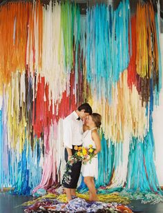 a man and woman standing in front of a multicolored backdrop with streamers