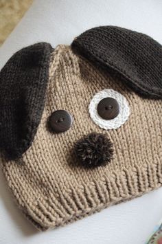 a knitted dog hat with buttons on the front and side, sitting on top of a pillow