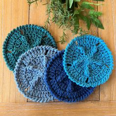 three crocheted scrubcloths sitting on top of a wooden floor next to a plant