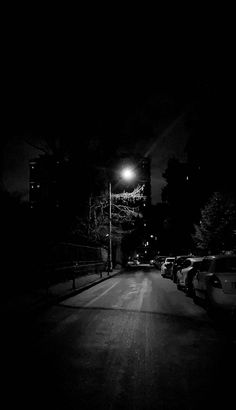 a dark street at night with cars parked on the side