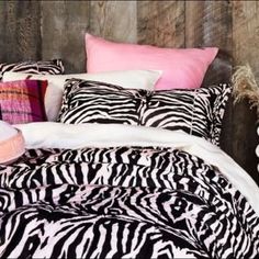 a zebra print comforter and pillows on a bed with wood headboard in the background