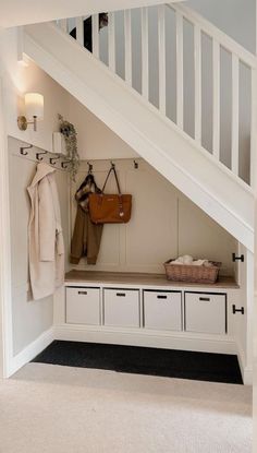 an entryway with white storage drawers under the stairs and a coat rack underneath it