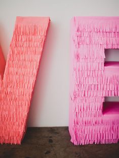 two pink letters with fringes on them are next to each other in front of a white wall