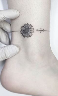 a sunflower tattoo on the ankle with an arrow in front of it that is attached to