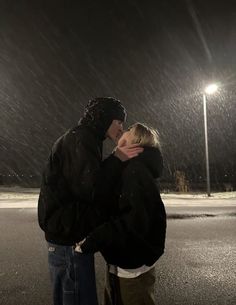 a man and woman standing in the rain under a street light at night with their arms around each other