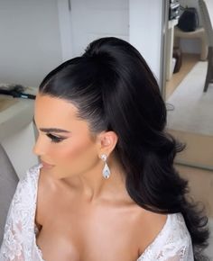 a woman with long black hair in a white dress and earrings sitting on a couch