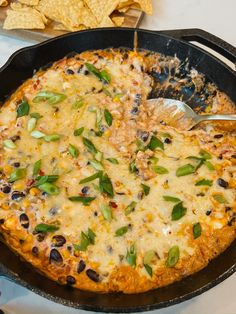 a skillet filled with cheese and black olives next to tortilla chips