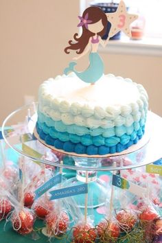 a little mermaid cake with blue and white frosting on the top is surrounded by candy candies