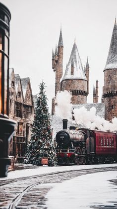 a train traveling past a tall castle like building with a christmas tree on the side